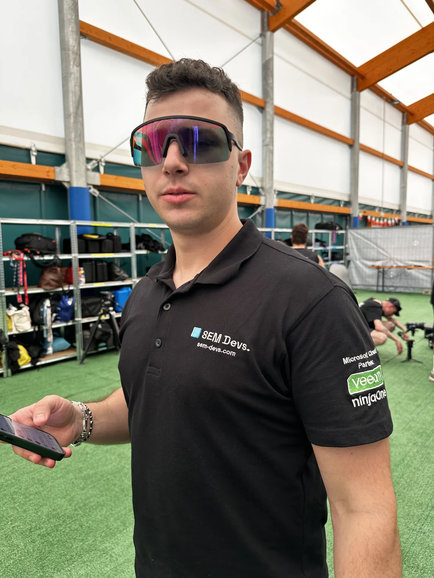 Un tecnico SEM Devs con polo brandizzata nel backstage della media crew del Nameless 2026, telefono in mano.